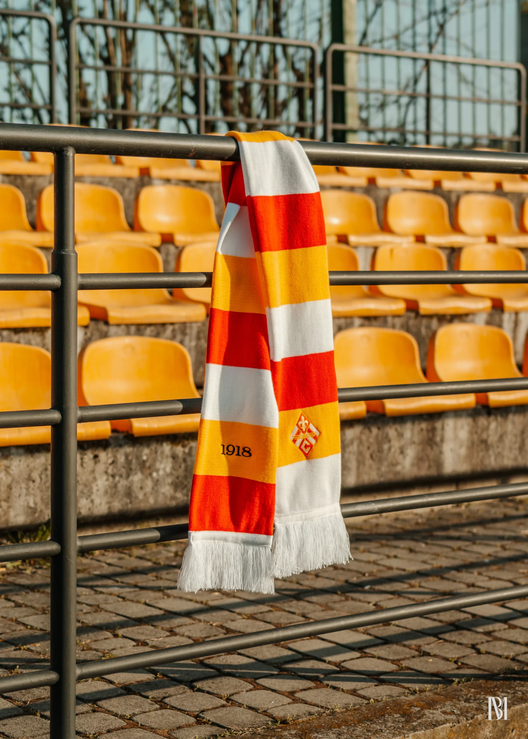 Szalik klubowy Czuwaj Przemyśl na tle krzesełek stadionowych w kolorach biało-żółto-czerwonych