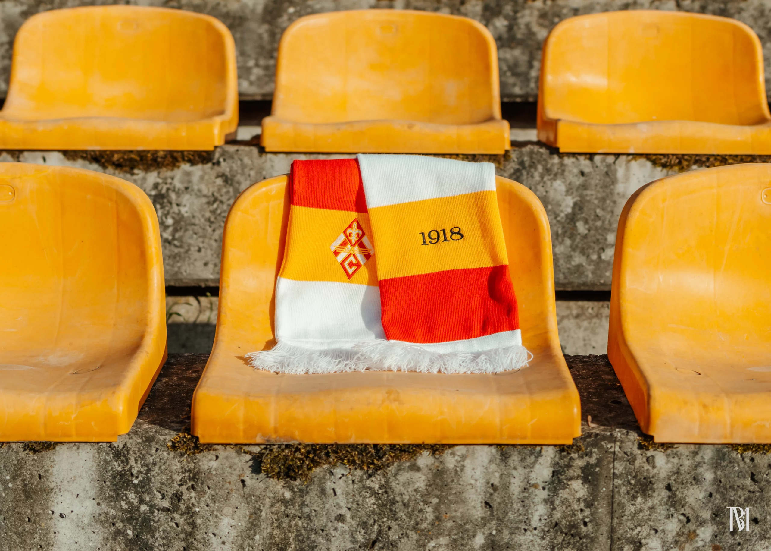 Szalik klubowy Czuwaj Przemyśl na tle krzesełek stadionowych w kolorach biało-żółto-czerwonych