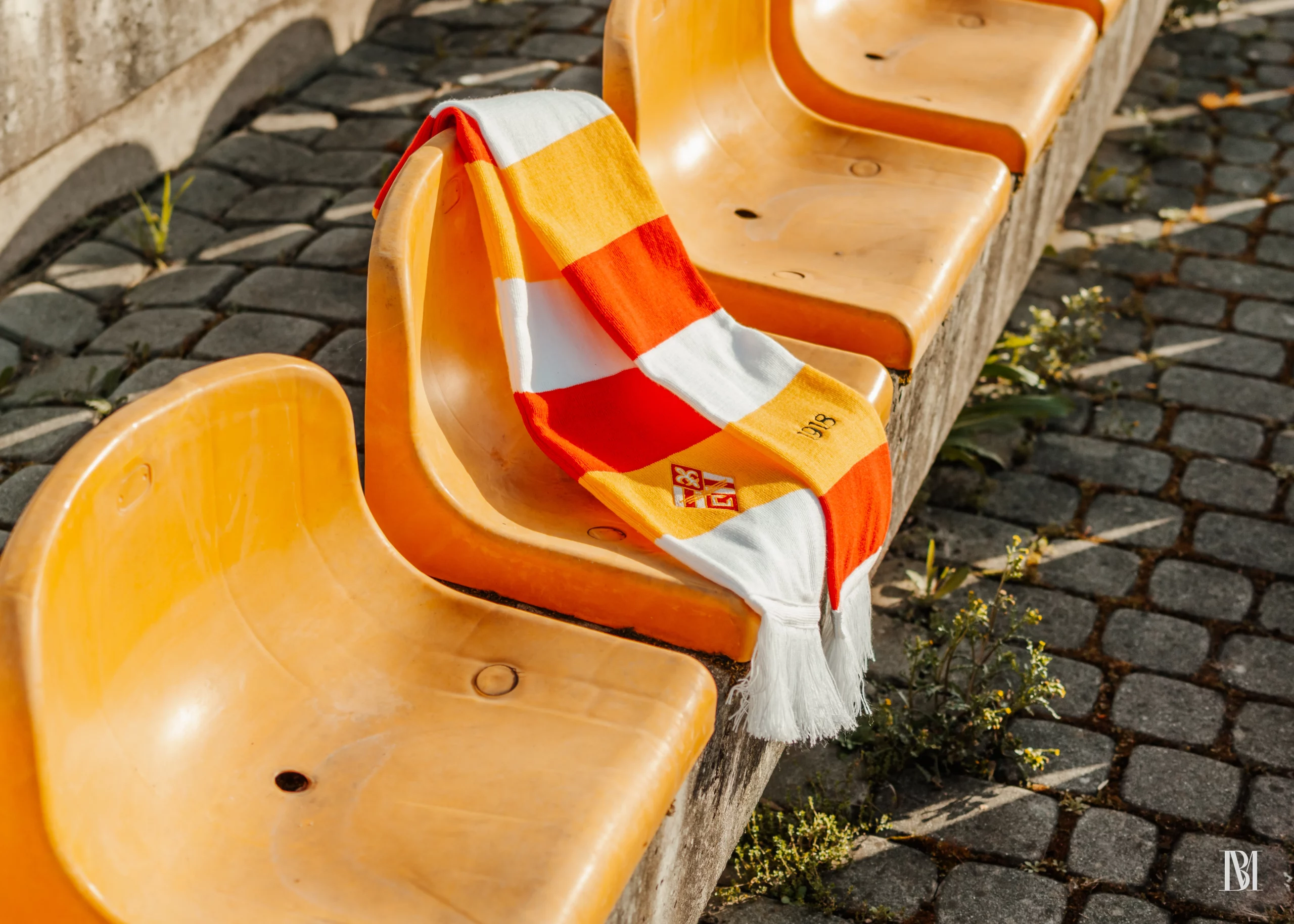 Szalik klubowy Czuwaj Przemyśl na tle krzesełek stadionowych w kolorach biało-żółto-czerwonych