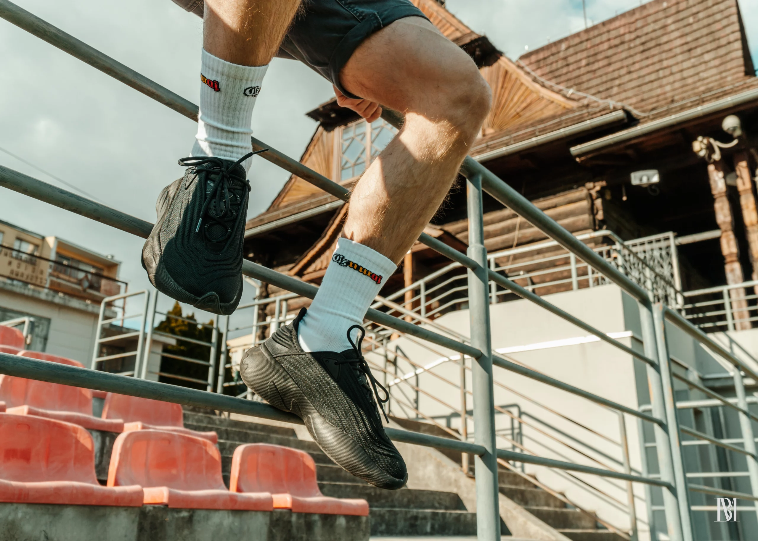 Białe skarpetki z mini flagą o kolorach biało-żółto-czerwonych i rokiem 1918 na tle stadionu, krzesełek i budynku klubowego.